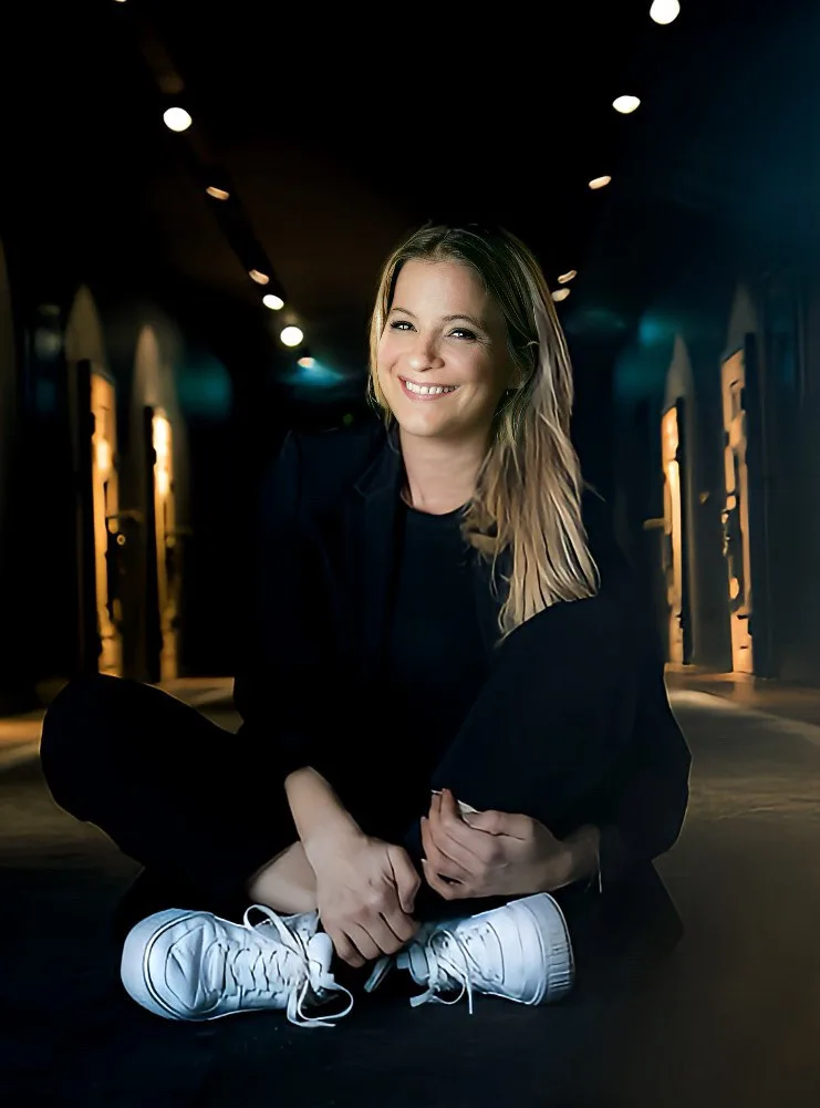 Rebecca Steinbach sitzt lächelnd im Schneidersitz in einem beleuchteten Gewölbegang